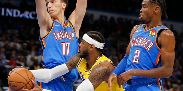Los Angeles Lakers forward Carmelo Anthony (7) goes against Oklahoma City Thunder forward Aleksej Pokusevski (17) and guard Shai Gilgeous-Alexander (2) during the first half of an NBA basketball game, Wednesday, Oct. 27, 2021, in Oklahoma City.
