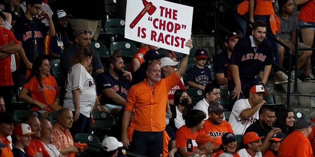 A fan holds a sign stating "the chop is racist" during the ninth inning in Game One of the World Series during the ninth inning at Minute Maid Park on October 26, 2021 in Houston, Texas.