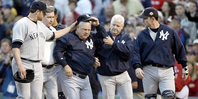 Bank coach Don Zimmer (center) of the New York Yankees is assisted by team coaches and pitcher Roger Clemens (left) after the excavation after Zimmer was thrown to the ground by Pedro Martinez of the Boston Red Sox after he charged Martinez during the fourth inning of Game 3 of the 2003 American League Championship Series on October 11, 2003 at Fenway Park in Boston, Massachusetts.