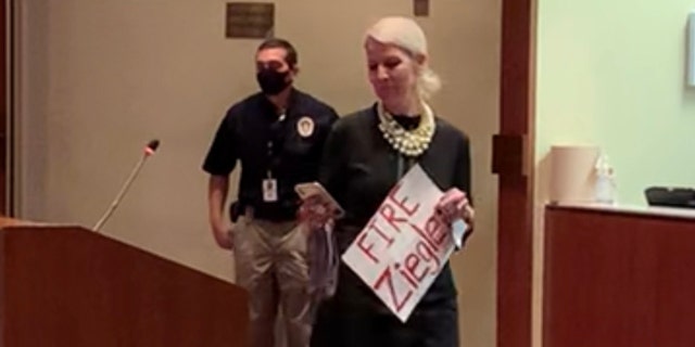 A Loudoun County mom enters a school board meeting with a sign reading "Fire Ziegler."