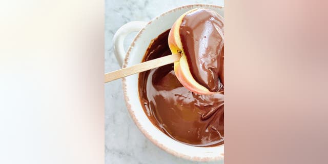 In jede Apfelscheibe muss ein Eiscreme-Stick eingeführt werden, bevor sie in geschmolzene Schokolade getaucht wird, gemäß dem deutschen Schokoladen-Karamell-Apfel-Rezept von Debi Morgan.