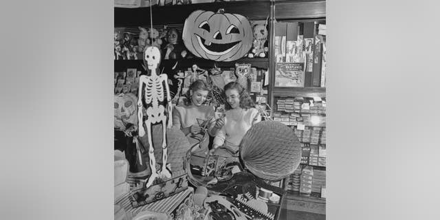 In this archive photo from the 1940s, two young women are shown examining a paper skeleton among other Halloween decorations.
