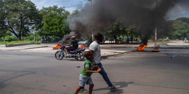A man and a child walk by burning tires on a street in Port-au-Prince, Haiti, Sunday, Oct. 17, 2021.