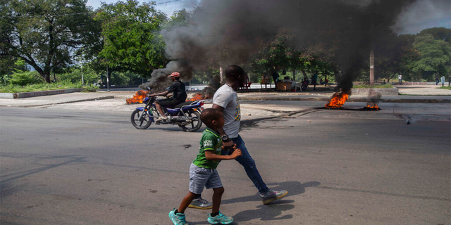 A man and a child walk, burning tires on a street in Port-au-Prince, Haiti on Sunday, October 17, 2021.
