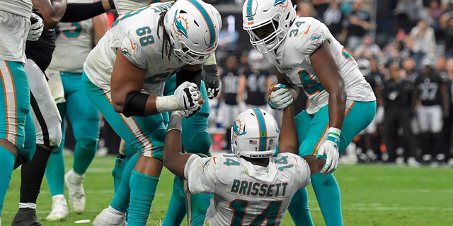 Miami Dolphins offensive guard Robert Hunt (68) and running back Malcolm Brown (34) help up quarterback Jacoby Brissett (14) after Brissett scored a touchdown against the Las Vegas Raiders during the second half of an NFL football game, Sunday, Sept. 26, 2021, in Las Vegas.