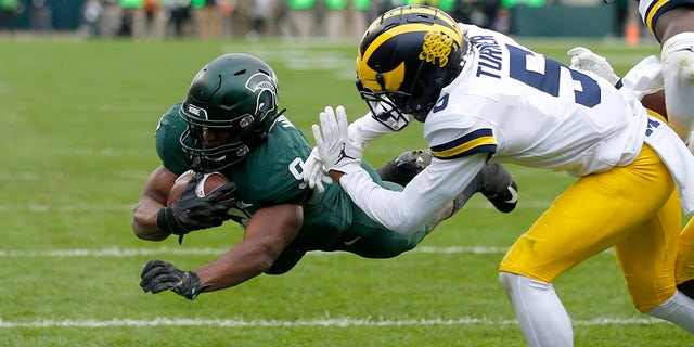 Michigan State's Kenneth Walker III, left, dives over the goal line for a touchdown against Michigan's DJ Turner during the second quarter Saturday, Oct. 30, 2021, in East Lansing, Mich.