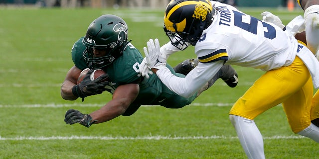 Michigan State's Kenneth Walker III, left, dives over the goal line for a touchdown against Michigan's DJ Turner during the second quarter Saturday, Oct. 30, 2021, in East Lansing, Mich.