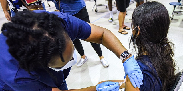 Een verpleegster geeft een meisje een dosis van het Pfizer-vaccin in een COVID-19-vaccinatiekliniek op een school. 