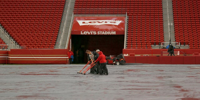Workers push water off a tarp covering the field from rain at Levi's Stadium before an NFL football game between the San Francisco 49ers and the Indianapolis Colts in Santa Clara, Kalifornië, Sondag, Okt.. 24, 2021. A powerful storm roared ashore Sunday in Northern California, flooding highways, toppling trees and causing mud flows as forecasters predict record-breaking rainfall.