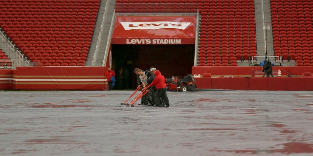 Workers push water off a tarp covering the field from rain at Levi's Stadium before an NFL football game between the San Francisco 49ers and the Indianapolis Colts in Santa Clara, Kalifornië, Sondag, Okt.. 24, 2021. A powerful storm roared ashore Sunday in Northern California, flooding highways, toppling trees and causing mud flows as forecasters predict record-breaking rainfall.