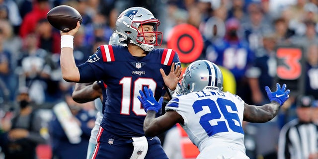 O quarterback do New England Patriots, Mac Jones (10), lança o cornerback do Dallas Cowboys, Jordan Lewis (26), no primeiro tempo de domingo, 17 de outubro de 2021, em Foxborough, Massachusetts.