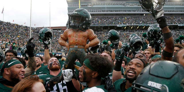 Michigan State players celebrate with the Paul Bunyan trophy defeating Michigan in an NCAA college football game, Saturday, Oct. 30, 2021, in East Lansing, Mich. Michigan State won 37-33.