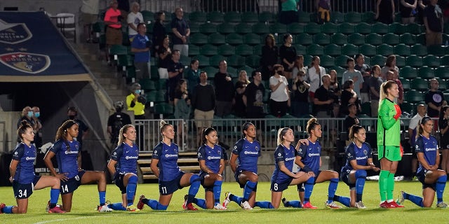 North Carolina Courage players take a knee during the national anthem prior to the team's NWSL soccer match against Racing Louisville FC in Cary, N.C., Wednesday, Oct. 6, 2021.