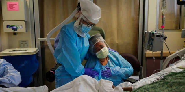FILE - In this July 31, 2020, file photo, Romelia Navarro, right, is comforted by nurse Michele Younkin as she weeps while sitting at the bedside of her dying husband, Antonio, in St. Jude Medical Center's COVID-19 unit in Fullerton, Calif. California's coronavirus death toll reached 70,000 people, on Monday, Oct. 11, 2021. 