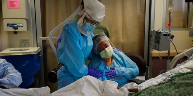 FILE - In this July 31, 2020, file photo, Romelia Navarro, right, is comforted by nurse Michele Younkin as she weeps while sitting at the bedside of her dying husband, Antonio, in St. Jude Medical Center's COVID-19 unit in Fullerton, Calif. California's coronavirus death toll reached 70,000 people, on Monday, Oct. 11, 2021. 