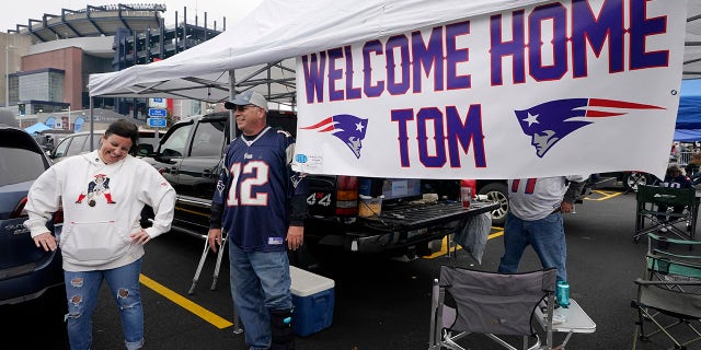 New England Patriots fan Stephanie Lamontagne, left, of Merrimack, N.H., smiles while chatting with Bill Gately, of Burrillville, R.I., while tailgating near a sign greeting the return of quarterback Tom Brady prior to a game between the New England Patriots and Tampa Bay Buccaneers, Sunday, Oct. 3, 2021, in Foxborough, Mass.