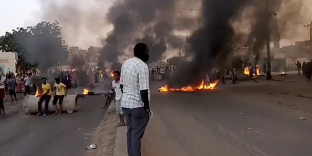 People gathering as fire and smoke are seen on the streets of Kartoum, Sudan, amid reports of a coup Monday.