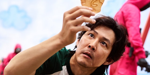 The third episode of the South Korean drama is titled "The man with the umbrella." Here you see the protagonist of the series Seong Gi-hun (played by Lee Jung-jae) examining his dalgona candy, which has an umbrella printed on it.