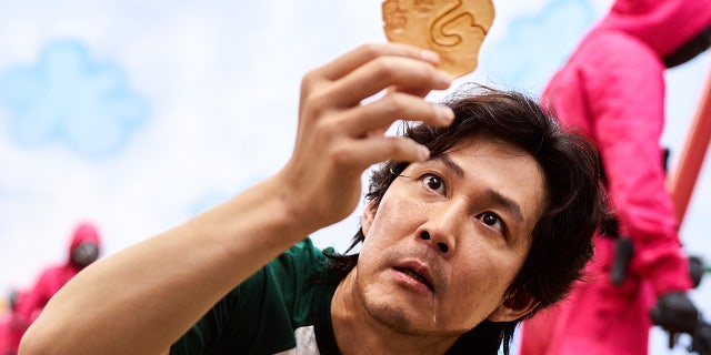 The third episode of the South Korean drama is titled "The man with the umbrella." Here you see the protagonist of the series Seong Gi-hun (played by Lee Jung-jae) examining his dalgona candy, which has an umbrella printed on it.