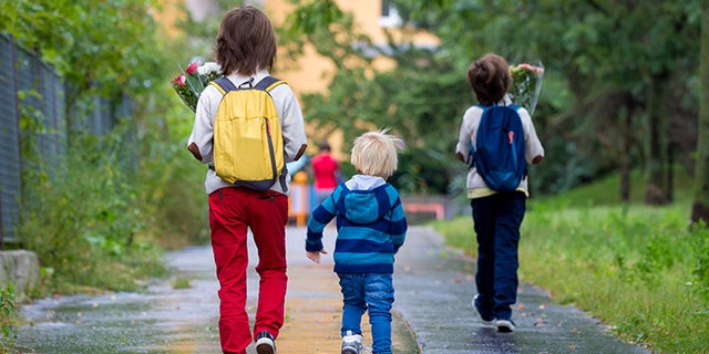 Happy school children, holding bouquet of flowers, going to school first day, rainy autumn day in September