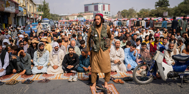 A Taliban fighter in the foreground and a group of Afghan men attend Friday prayers in Kabul, Afghanistan on Friday, September 24, 2021.