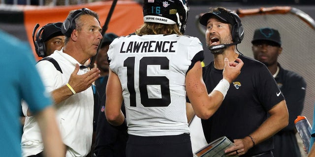 Trevor Lawrence of the Jacksonville Jaguars meets with head coach Urban Meyer and coach Brian Schottenheimer against the Bengals at Paul Brown Stadium on Sept. 30, 2021, in Cincinnati, Ohio.