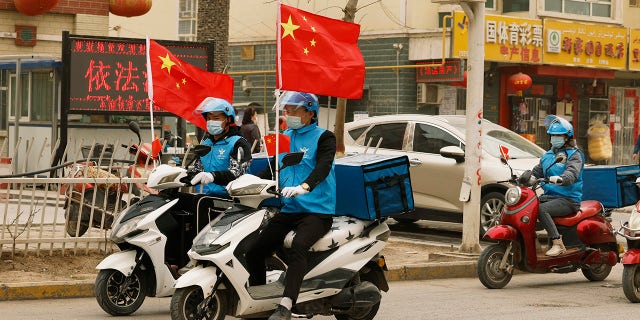 Delivery workers flying Chinese national flags ride around in a convoy to promote their services in Shule county in northwestern China's Xinjiang Uyghur Autonomous Region on March 20, 2021.