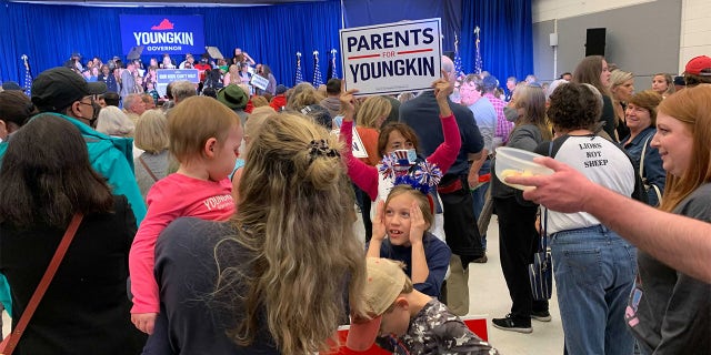 A girl plays peekaboo with a baby at a Glenn Youngkin rally.