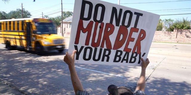 David Trujillo holds a sign as a school bus drives by on the street in front of a building housing an abortion provider in Dallas, Thursday, Oct. 7, 2021. (AP Photo/LM Otero)