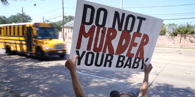 David Trujillo holds a sign as a school bus drives by on the street in front of a building housing an abortion provider in Dallas, Thursday, Oct. 7, 2021. (AP Photo/LM Otero)