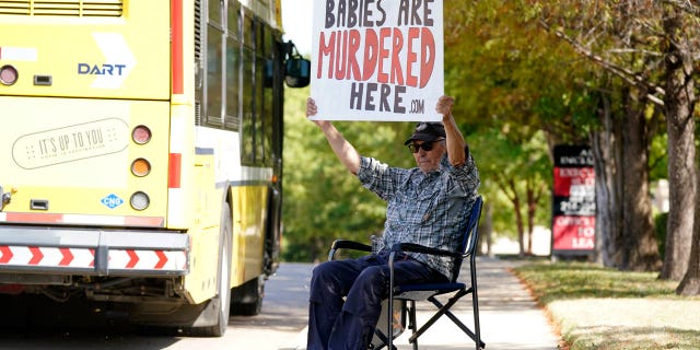 David Trujillo holds a sign as a bus drives down the street in front of a building housing an abortion provider in Dallas on Thursday, October 7, 2021. A federal judge has ordered Texas to suspend a new law that bans most abortions in the state since September.  A federal appeals court restored the law on Friday night.