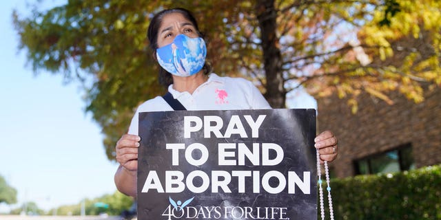 Maria Peña holds a rosary and sign out outside a building housing an abortion provider in Dallas, Thursday, Oct. 7, 2021.