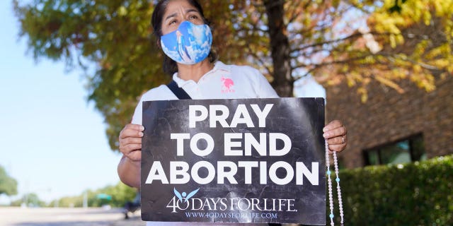 Maria Peña holds a rosary and sign out outside a building housing an abortion provider in Dallas, Oct. 7, 2021.