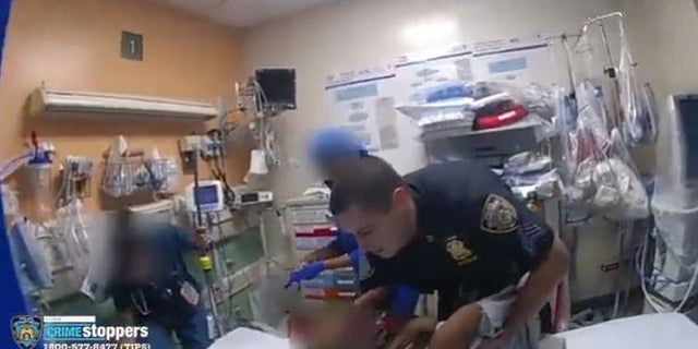 An NYPD officer holds a child and lays him down in a Brooklyn hospital. 