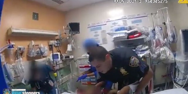 An NYPD officer holds a child and lays him down in a Brooklyn hospital.