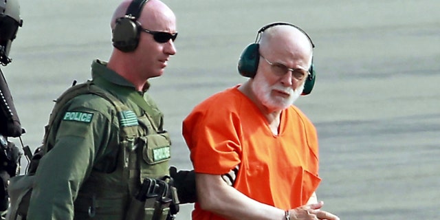 Whitey Bulger wearing headphones and a prison jumpsuit as he's escorted from a U.S. Coast Guard helicopter