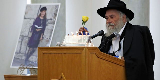 In this April 29, 2019, file photo, Yisroel Goldstein, Rabbi of Chabad of Poway, holds a yellow rose as he speaks at the funeral for Lori Kaye, who is pictured at left, in Poway, Calif. Kaye, who was was killed April 27, 2019, when a gunman opened fire inside the Chabad of Poway synagogue, had given Goldstein the flower as part of a bouquet the day before the shooting, which also injured Goldstein. (AP Photo/Gregory Bull, File)