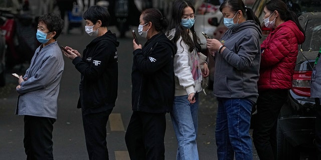 A woman wearing a face mask to help curb the spread of the coronavirus walks through a line of masked service sector women waiting to receive a swab for the COVID-19 test during a mass test in Beijing on Friday, following a a peak of the coronavirus in the capital and other provinces. 