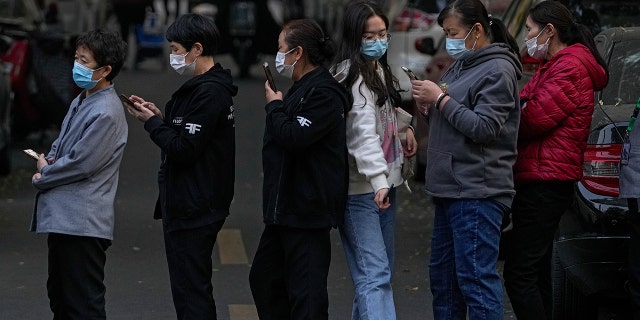 A woman wearing a face mask to help curb the spread of the coronavirus walks through a line of masked service sector women waiting to receive a swab for the COVID-19 test during a mass test in Beijing on Friday, following a a peak of the coronavirus in the capital and other provinces.