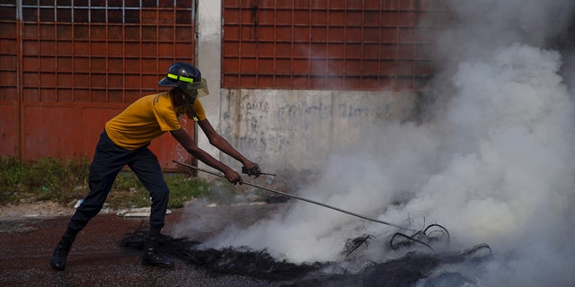 A firefighter puts out a smoldering road block set by protesters in Port-au-Prince, Haiti, on Monday. 