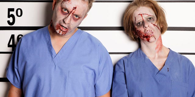 A mugshot/booking photo of a woman and man dressed as a zombies.
