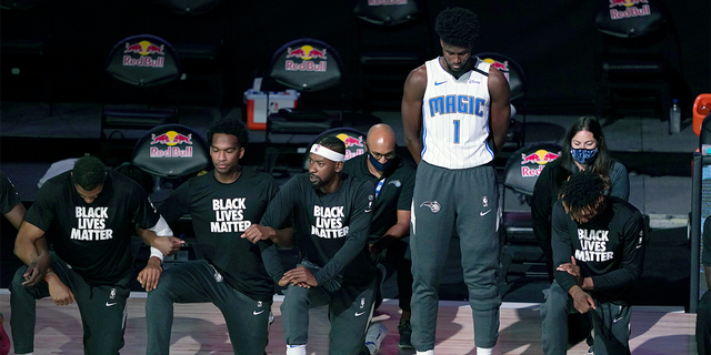 LAKE BUENA VISTA, FL - JULY 31: Orlando Magic No.1 Jonathan Isaac stands as others kneel before the start of a game between the Brooklyn Nets and the Orlando Magic on July 31, 2020 at the HP Field House at ESPN Wide World Of Sports Complex in Lake Buena Vista, Florida.  (Photo by Ashley Landis - Pool / Getty Images)