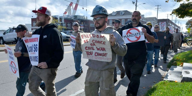 Justin Paetow, center, a tin shop worker at Bath Iron Works, takes part in a demonstration against COVID-19 vaccine mandate outside the shipyard on Friday, Oct. 22, 2021, in Bath, Maine. (AP Photo/Josh Reynolds)
