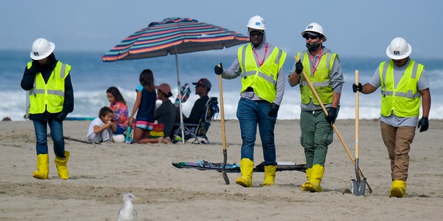 In this photo from Oct. 11, 2021, a family is under an umbrella as workers continue to clean the contaminated beach in Huntington Beach, California.
