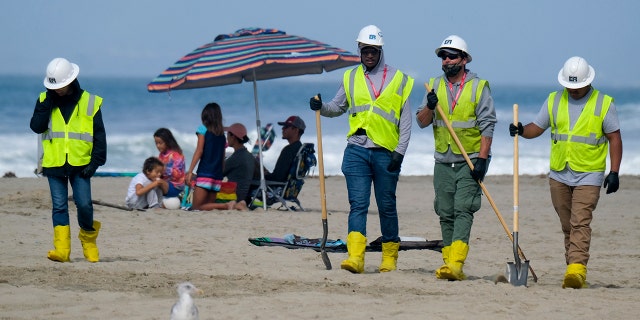 In this photo from Oct. 11, 2021, a family is under an umbrella as workers continue to clean the contaminated beach in Huntington Beach, 캘리포니아.