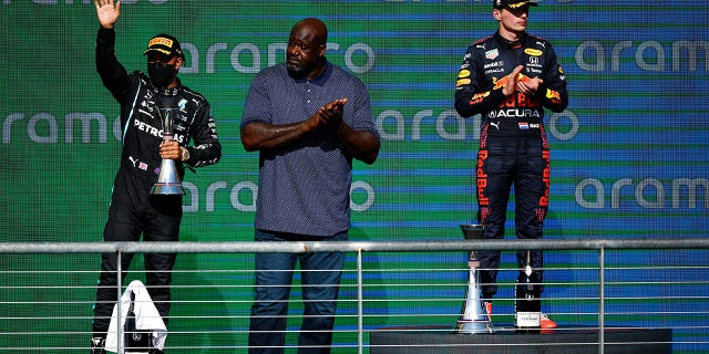 Shaquille O'Neal stands between Lewis Hamilton (L) and U.S. Grand Prix winner Max Verstappen on the Circuit of the Americas winner's stand.