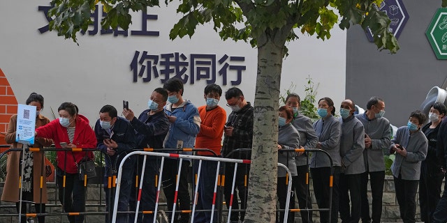 Service sector workers line up for a COVID-19 test during a mass testing at a site baring the words, "You and me on the road of civilization" in Beijing on Friday, following a spike of the coronavirus in the capital and other provinces.