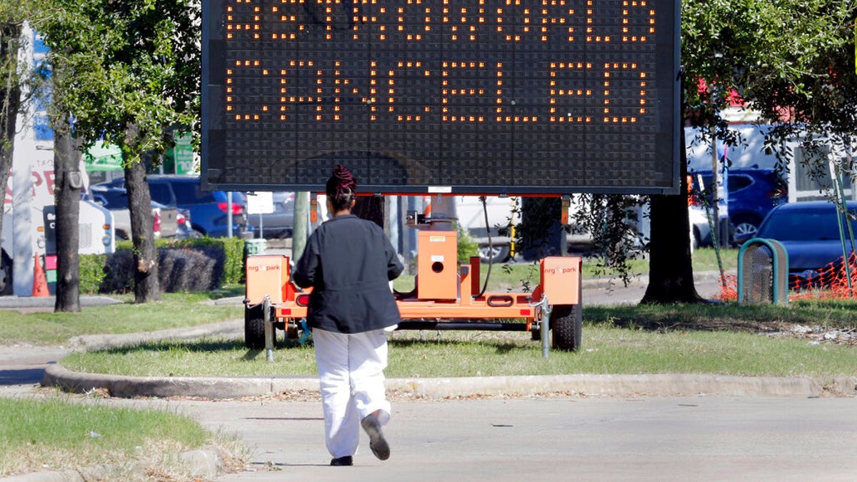A pedestrian cross Main Street in front of a sign announcing the cancellation of Astroworld on Saturday, Nov. 6, 2021, in Houston. Several people died and numerous others were injured in what officials described as a surge of the crowd at the music festival while Travis Scott was performing Friday night.  