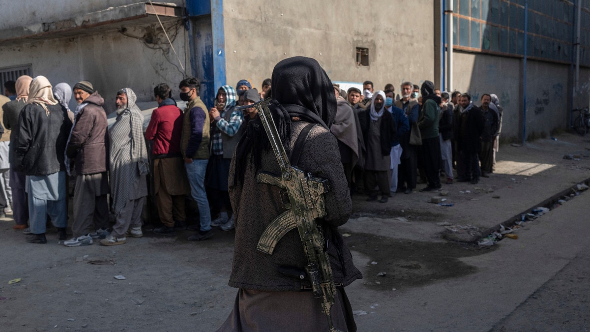 A Taliban fighter secures the area as people queue to receive cash at a money distribution organized by the World Food Program (WFP) in Kabul, Afghanistan, on Wednesday , Nov. 17, 2021. (AP Photo/ Petros Giannakouris)