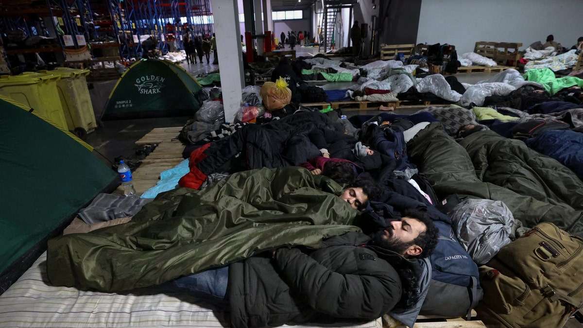 Migrants sleep inside a logistics center at the checkpoint "Kuznitsa" at the Belarus-Poland border near Grodno, Belarus, Sunday, Nov. 21, 2021. The EU says the new surge of migrants on its eastern borders has been orchestrated by the leader of Belarus, President Alexander Lukashenko, in retaliation for EU sanctions placed on Belarus after a government crackdown on peaceful democracy protesters. It calls the move "a hybrid attack'' on the bloc. Belarus denies the charge. (Maxim Guchek/BelTA via AP)